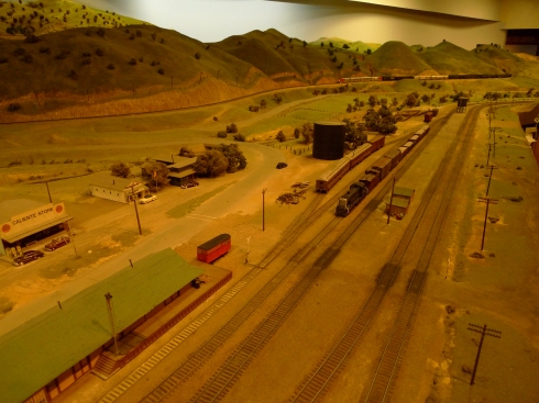 A local freight switches the town of Caliente, while a Santa Fe Passenger train drifts downgrade into town to pass. This is also part of the huge La Mesa Model Railroad Club in 1/87 scale (HO Gauge) layout circa 1952. The club models the Tehachapi Loop area of California. The club is in located near San Diego, CA USA.
